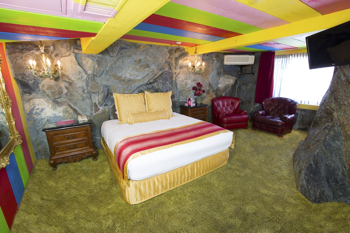 Ein Zimmer mit einem Bett, einem roten Ledersessel, einem kleinen Tisch mit einer Vase und einer Steinwand.