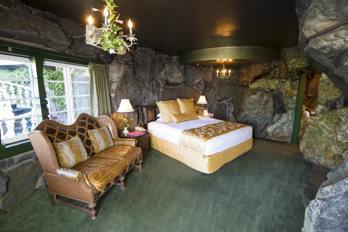 Ein Schlafzimmer mit Steinwand, einem Bett, einer Couch und einer Pendelleuchte.