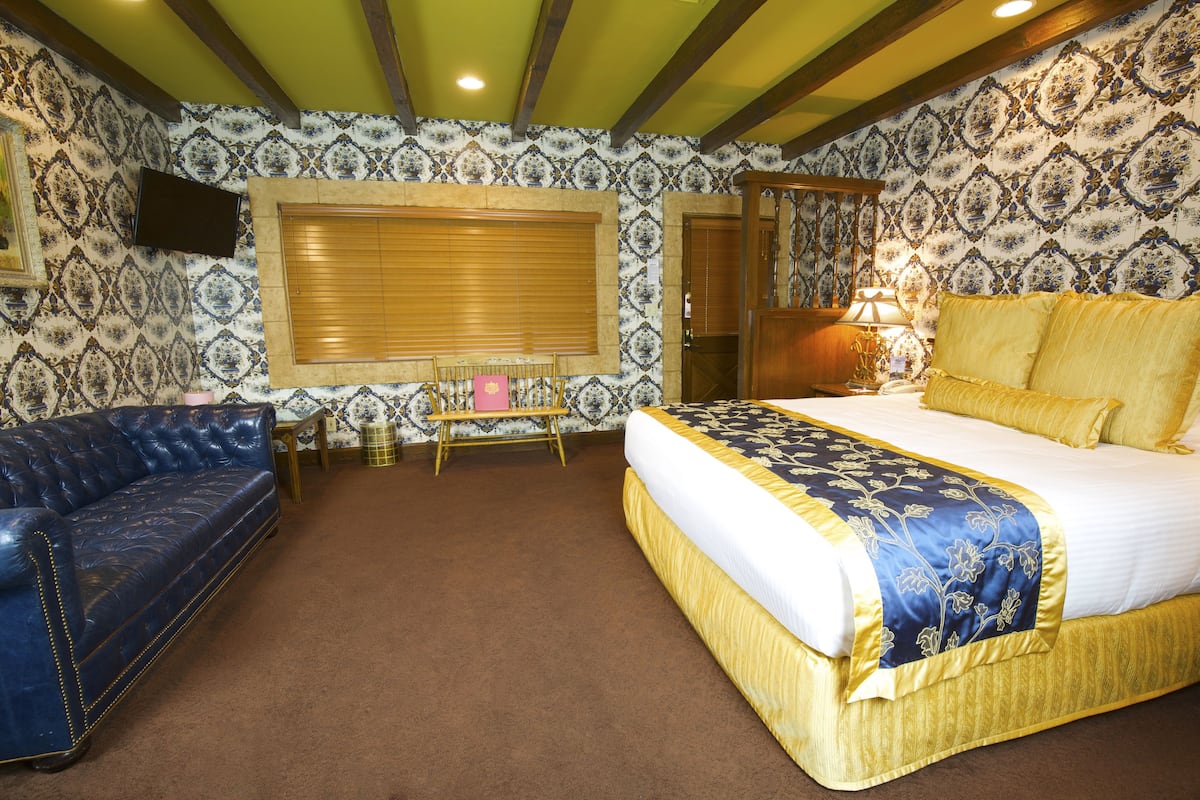 Ein Schlafzimmer mit einem großen Bett, einem blauen Sofa, einem Holzstuhl, einem kleinen Tisch und einem Fernseher an der Wand.