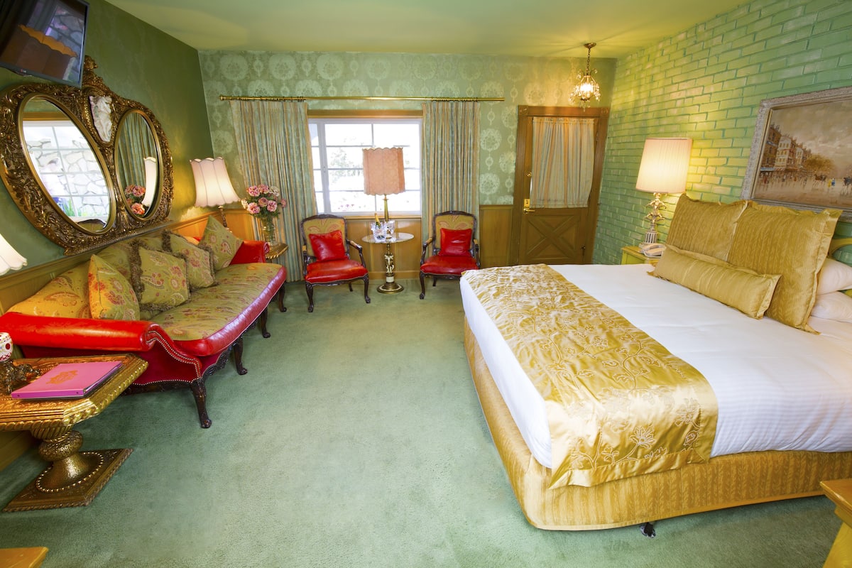 Ein Hotelzimmer mit einem großen Bett, zwei Sesseln, einem kleinen Tisch und einem Spiegel.