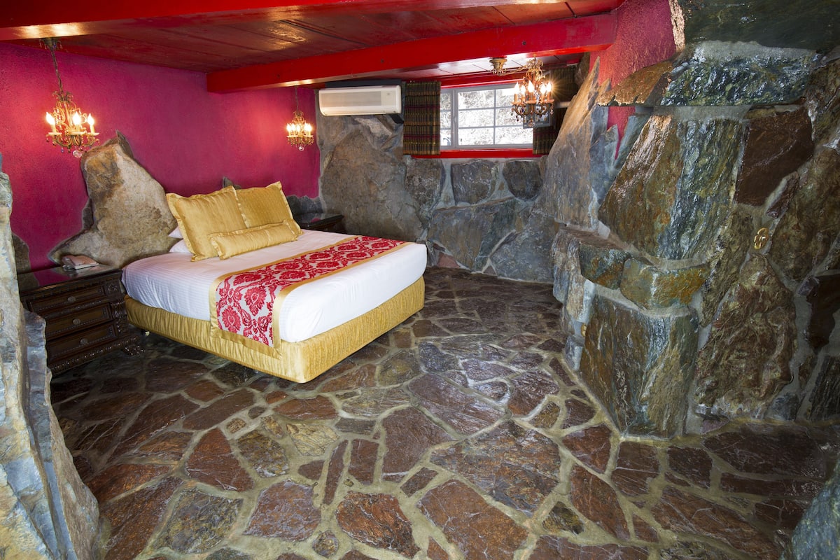 Ein Schlafzimmer mit Steinfußboden, einem Bett mit rotem und weißem Überwurf und einer Steinsturzwand.