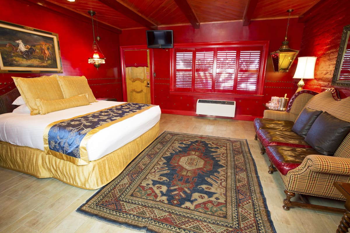 Ein Zimmer mit einem Bett, einem Schlafsofa, einem Teppich, einem Fernseher und einem Fenster mit Rollläden.