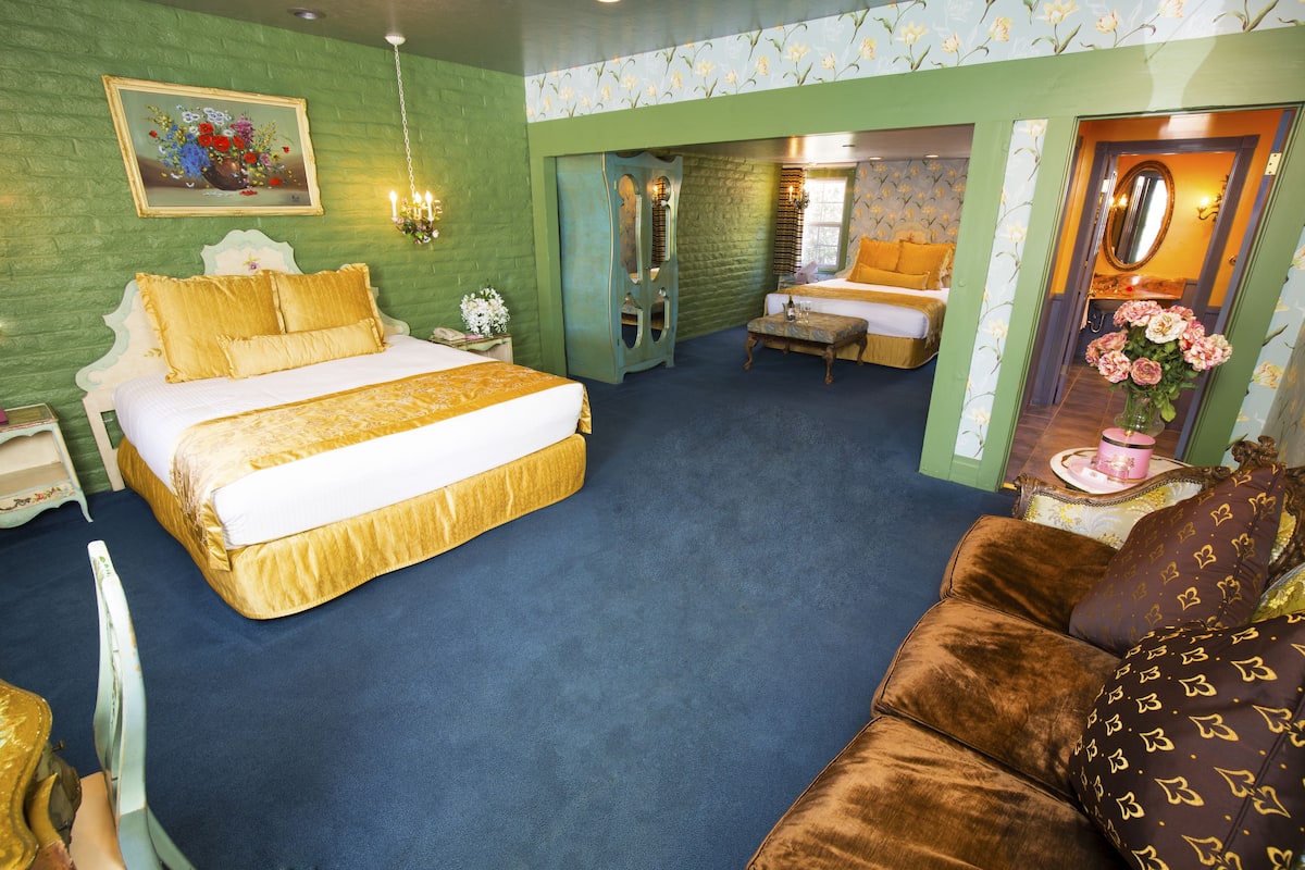 Ein Hotelzimmer mit einem großen Bett, einer Couch, einem kleinen Tisch mit Blumenvase und einem Spiegel.