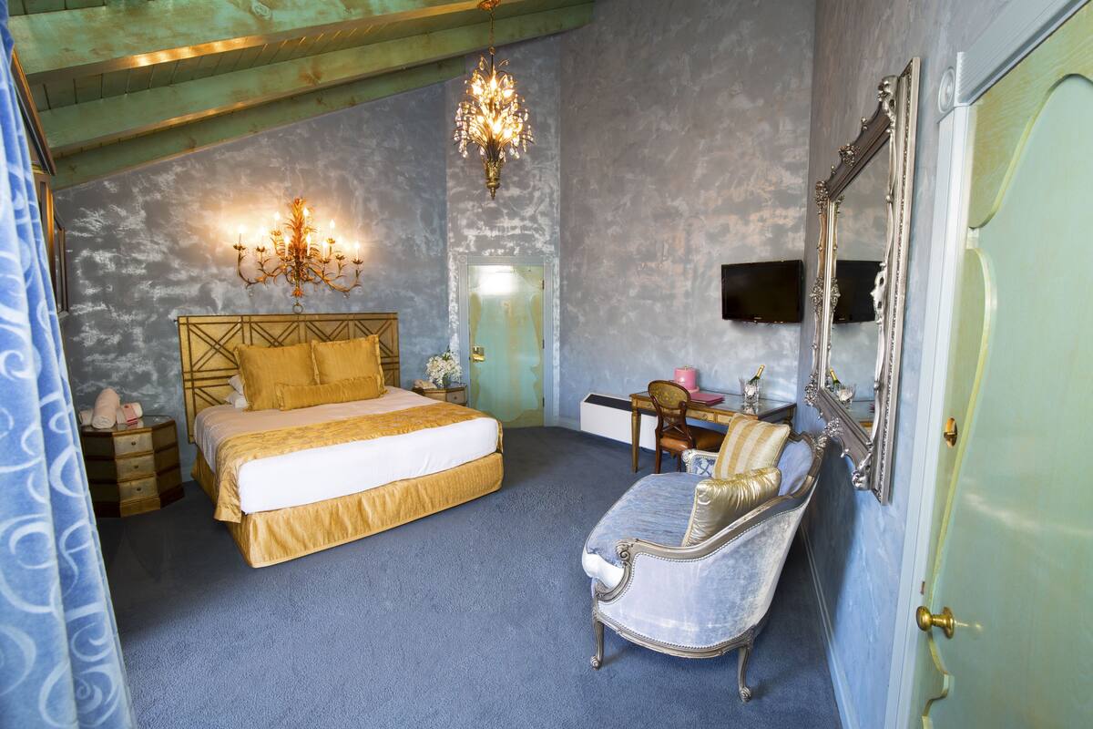 Ein Schlafzimmer mit einem großen Bett, einem Schminktisch mit Spiegel, einer Kristallleuchtre und einem blauen Teppich.