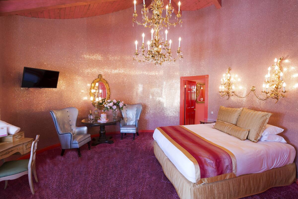 Ein Schlafzimmer mit einem großen Bett, einem Schreibtisch, einem Stuhl, einem Spiegel und einer Chandelieber.