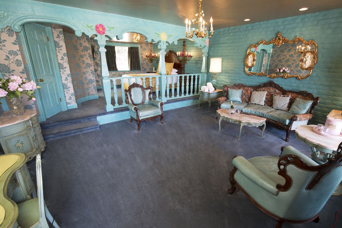 Ein stilvolles Zimmer im Vintage-Look mit blau-weißer Farbgebung, das antike Möbel, einen Chandelier und einen großen Spiegel beherbergt.