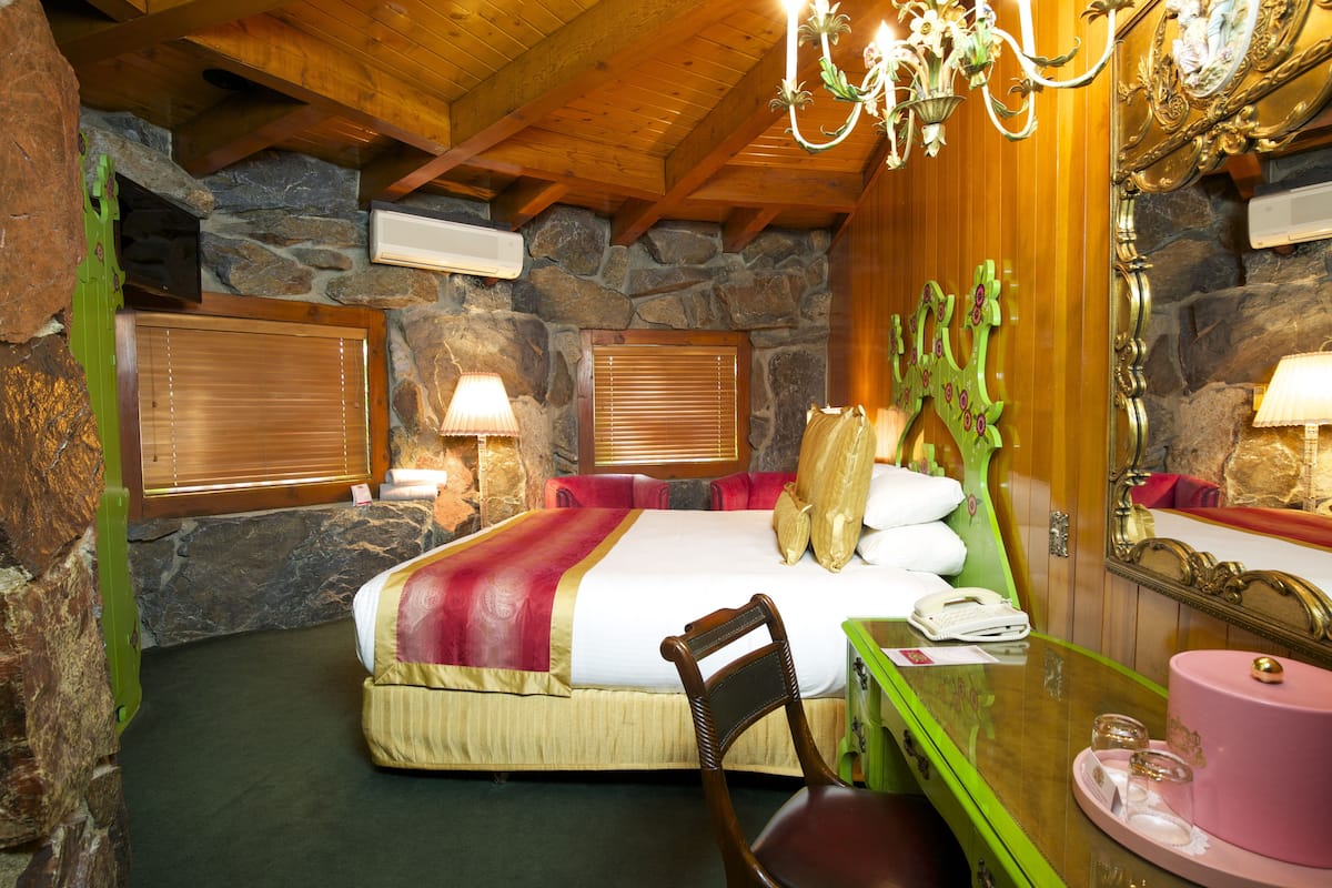 Ein Zimmer mit einem Bett, einem Schreibtisch, einem Stuhl, einem Spiegel und einer Kandelaber.