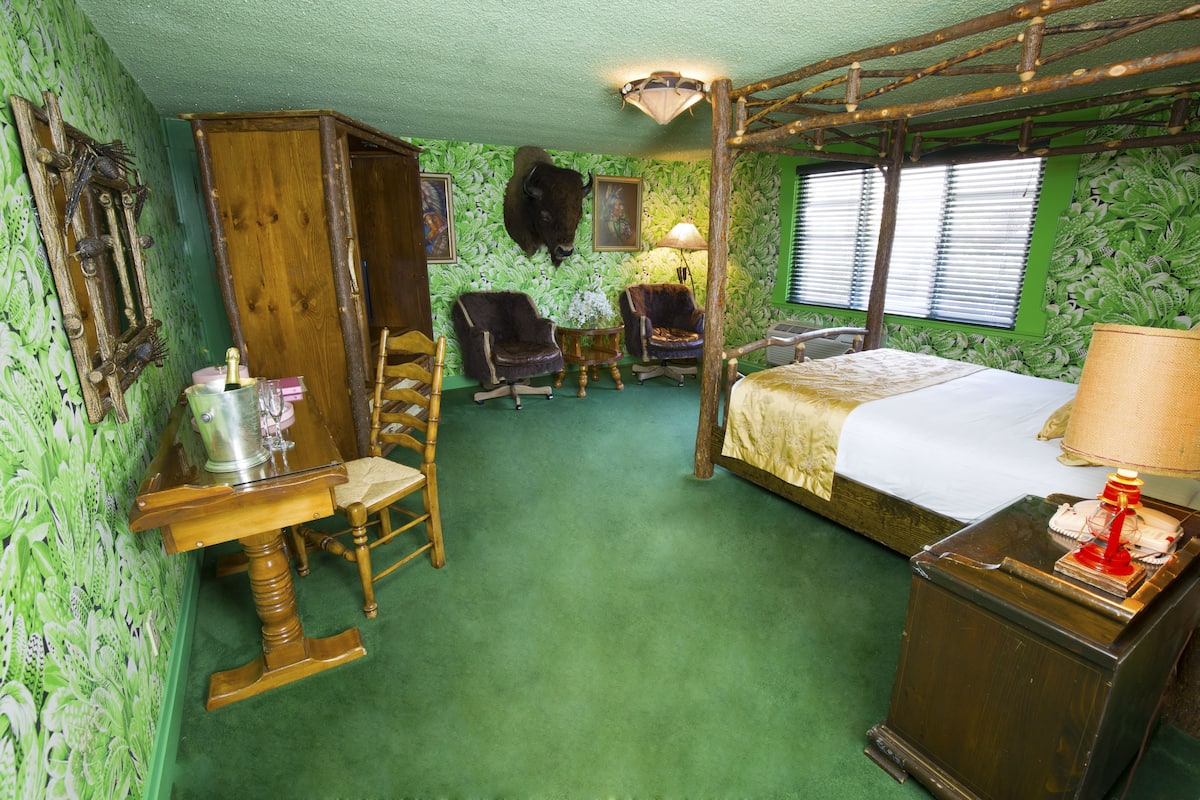 Ein Zimmer mit einem Bett, zwei Schaukelstühlen, einem Holztisch und einer Lampe.