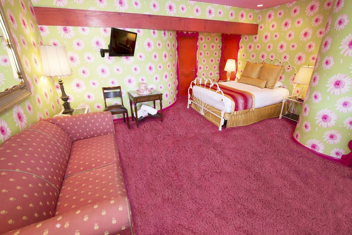 Ein Zimmer mit einem Bett, einem Sessel, einem kleinen Tisch und einem Spiegel.