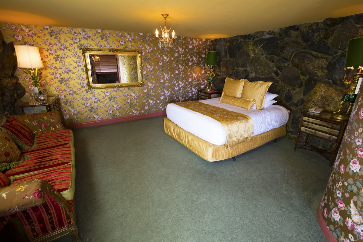 Ein Schlafzimmer mit einem großen Bett, einem Sessel, einem Nachttisch und einer Wand mit blumigem Tapetenmuster.