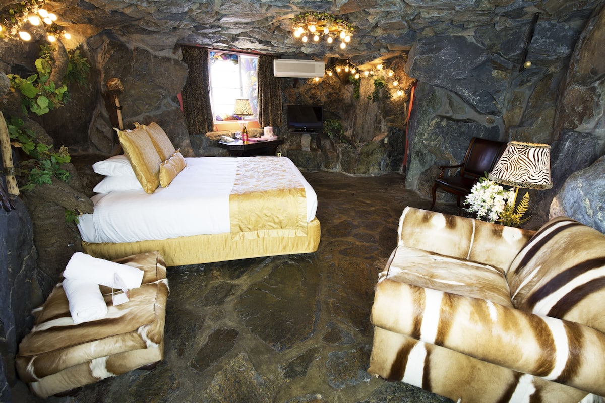 Ein Schlafzimmer mit Steinwänden, einem Bett, zwei Sofas, einem Fernseher und einer Lampe.