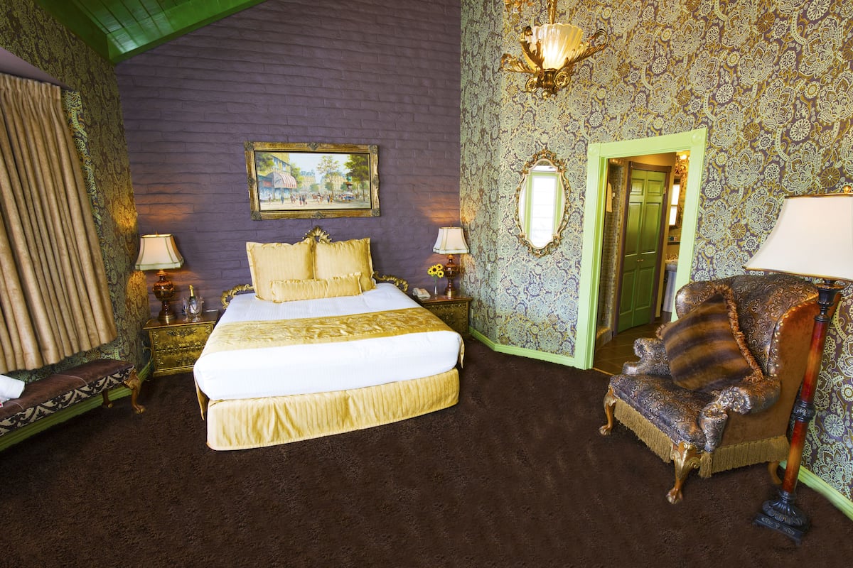 Ein Zimmer mit einem großen Bett, einem Sessel und einem Spiegel an der Wand.
