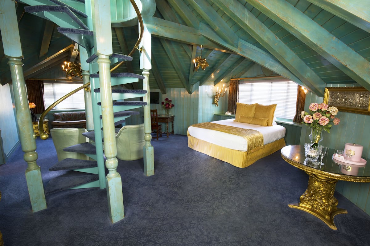 Ein Schlafzimmer mit einem großen Bett, einer Wendeltreppe und einem runden Tisch mit Blumen.