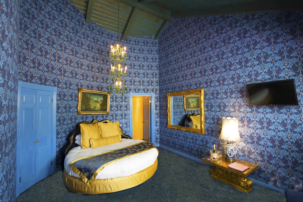 Ein Schlafzimmer mit einem großen Bett, einem Nachttisch mit Lampe, einem Spiegel und einer Tür.
