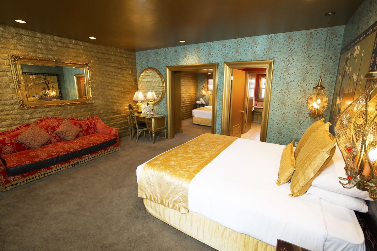 Ein Hotelzimmer mit einem großen Bett, einem roten Sofa, einem Schreibtisch mit Lampe und einem Spiegel an der Wand.