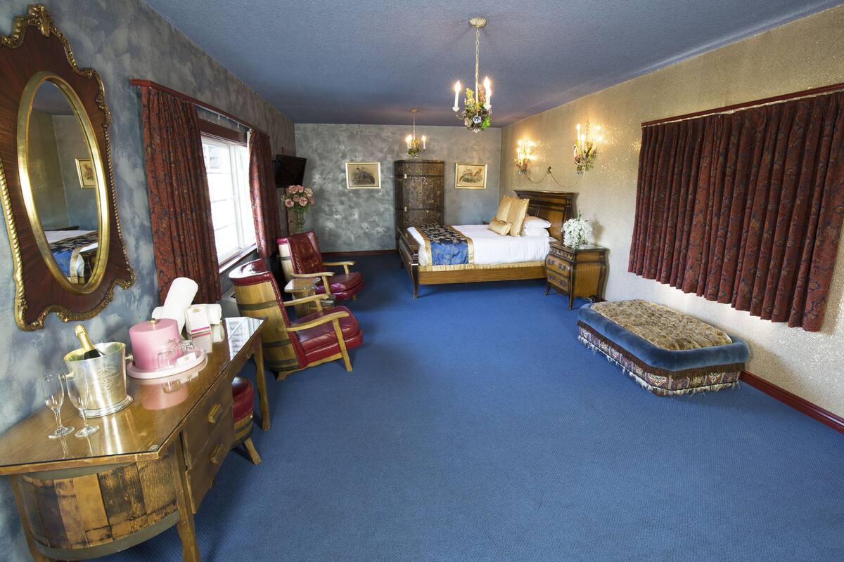 Ein Schlafzimmer mit einem großen Bett, einem Schminktischchen, einem Frisiertisch, einem Sessel, einem kleinen Tisch und einem Spiegel.
