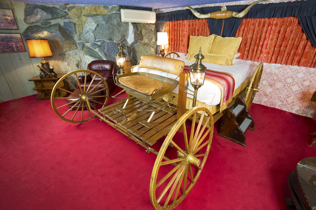 Ein Zimmer mit einem großen hölzernen Wagen, einem Bett mit rot-weißer Bettwäsche und einer Steinwand.