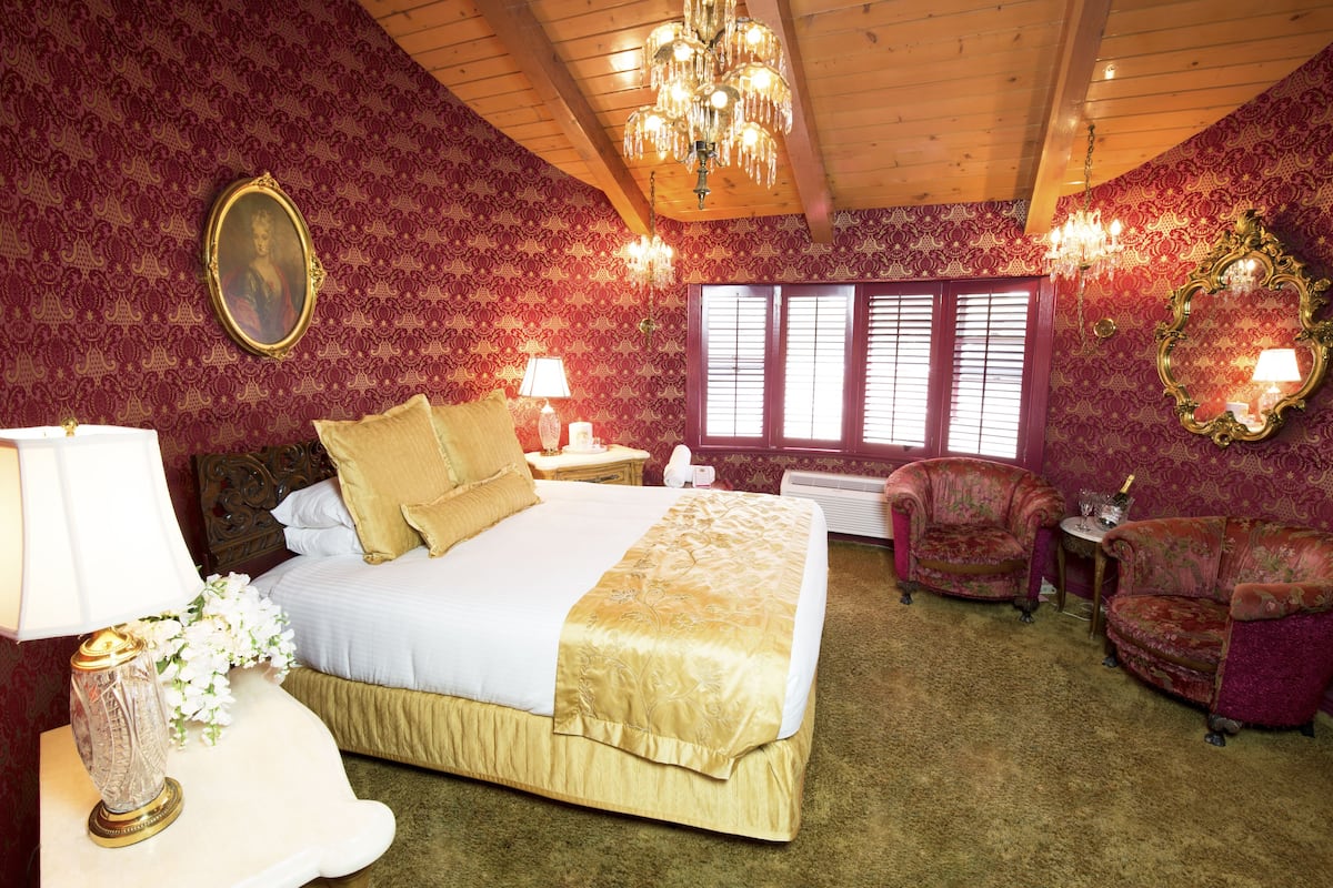 Ein Schlafzimmer mit einem großen Bett, zwei Nachttischen, einer Chandelier, einem Spiegel und einem Fenster mit Fensterläden.