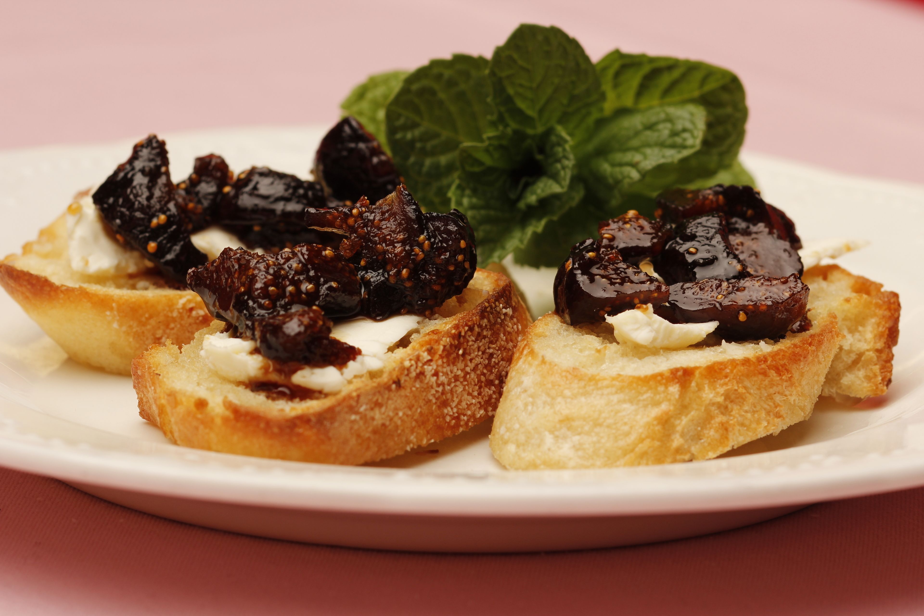 A plate with three pieces of toast topped with figs and a mint leaf.