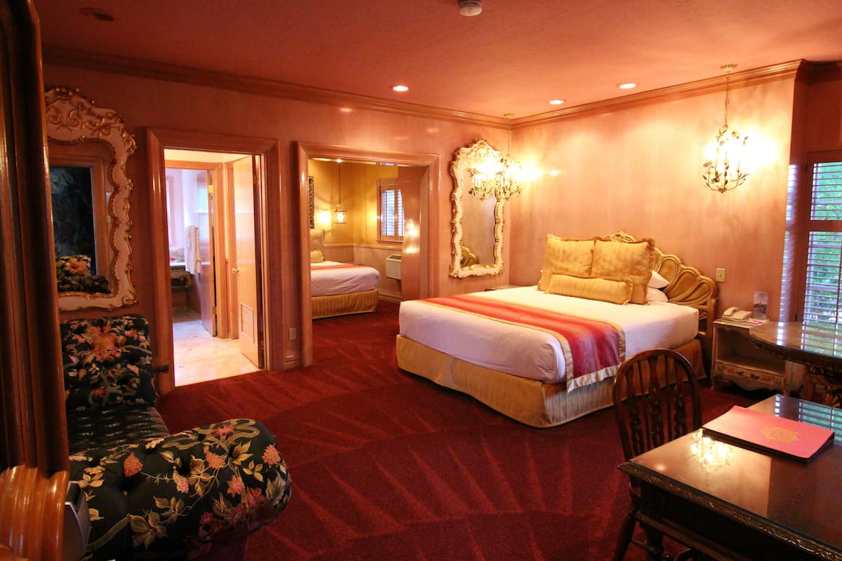 Ein Hotelzimmer mit einem großen Bett, einem Schreibtisch mit Stuhl, einem Spiegel und einer Chandelier.