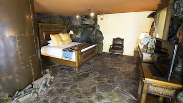 Une chambre au sol en pierre, avec un lit, une commode en bois et un mur en pierre.
