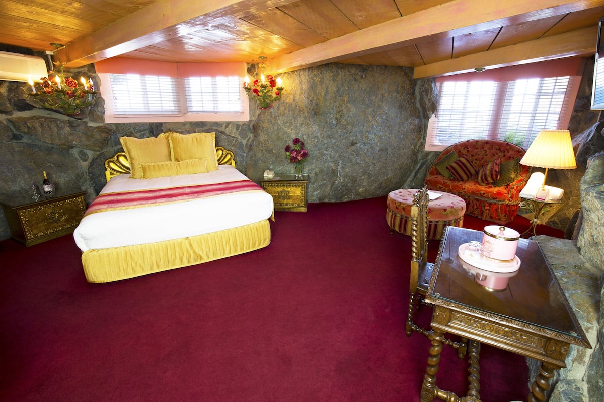 Ein Schlafzimmer mit einem großen Bett, einer Couch, einem Tisch und einer Steinwand.