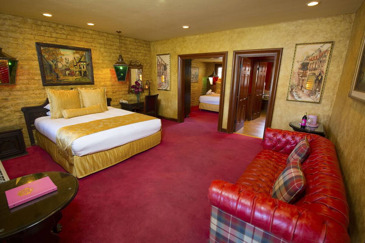 Ein Hotelzimmer mit einem großen Bett, einem roten Ledersofa und einem Schreibtisch mit einem Laptop.