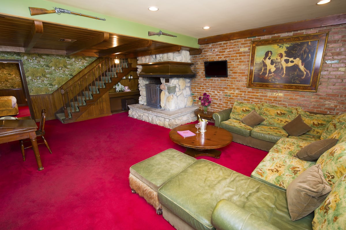 Ein Wohnzimmer mit Kamin aus Stein, einem grünen Sofa, einer Holztreppe und einem aufgehängten Gewehr.
