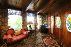 A cozy room with a stone wall, a red leather sofa, a wooden desk, and a stained glass window.