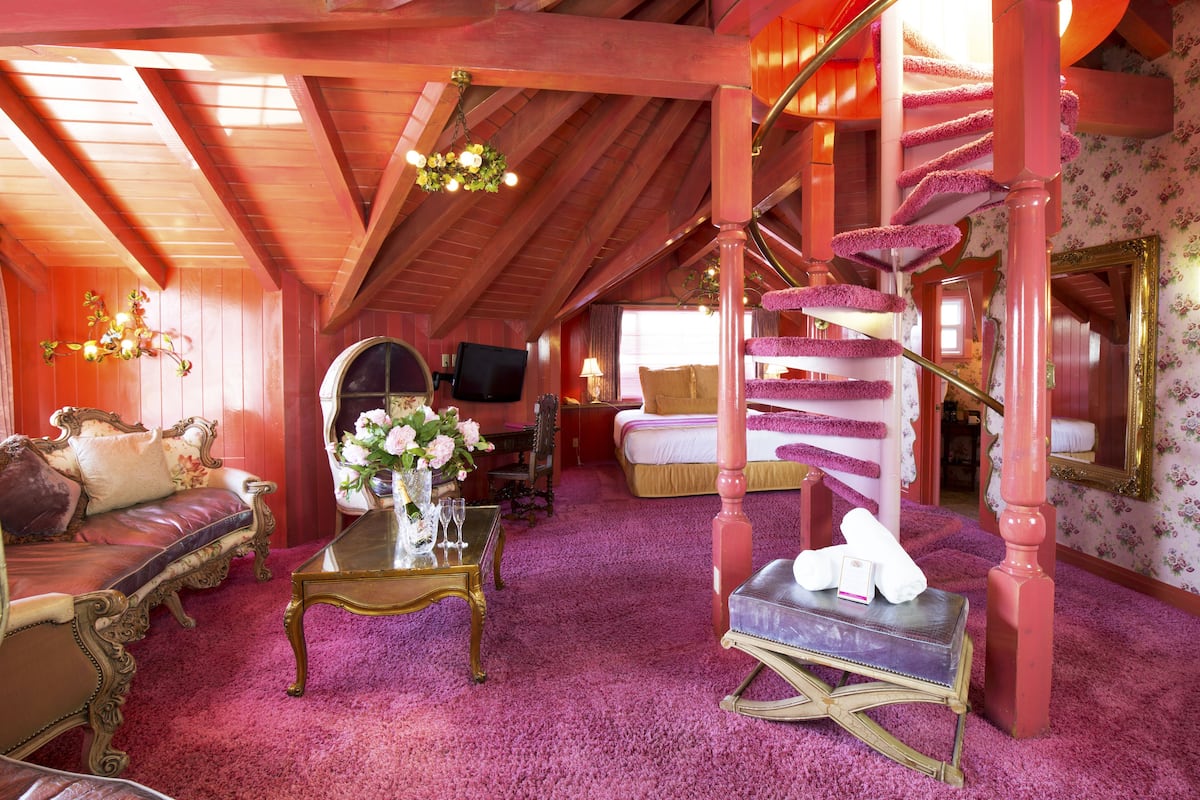 Ein Zimmer mit Holzboden, einer rosa Wendeltreppe, einem Bett mit weißer Bettdecke und einer Couch mit floralen Kissen.