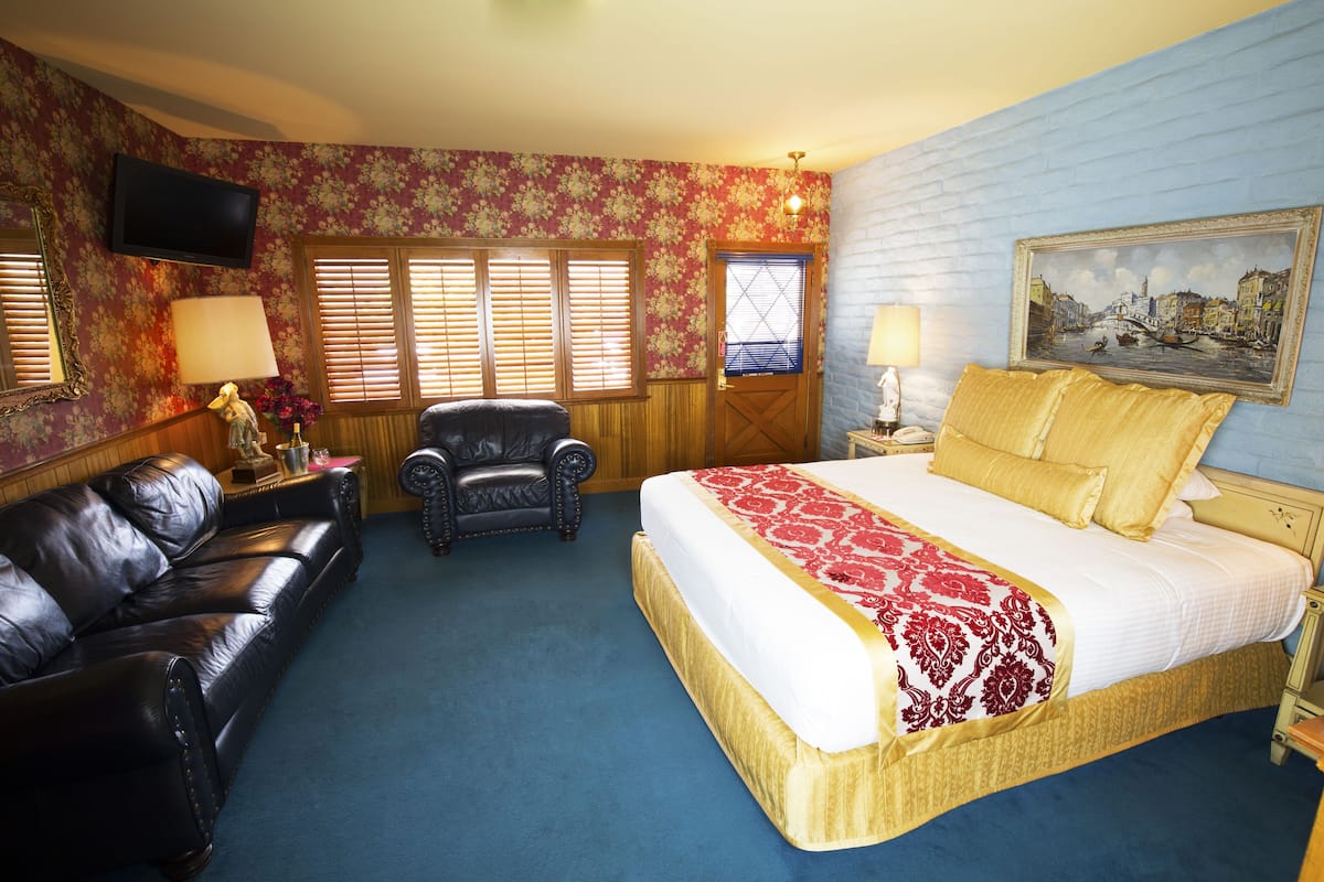 Ein Hotelzimmer mit einem großen Bett, einer Ledersofa, einem Holzsessel und einem an der Wand befestigten Fernseher.