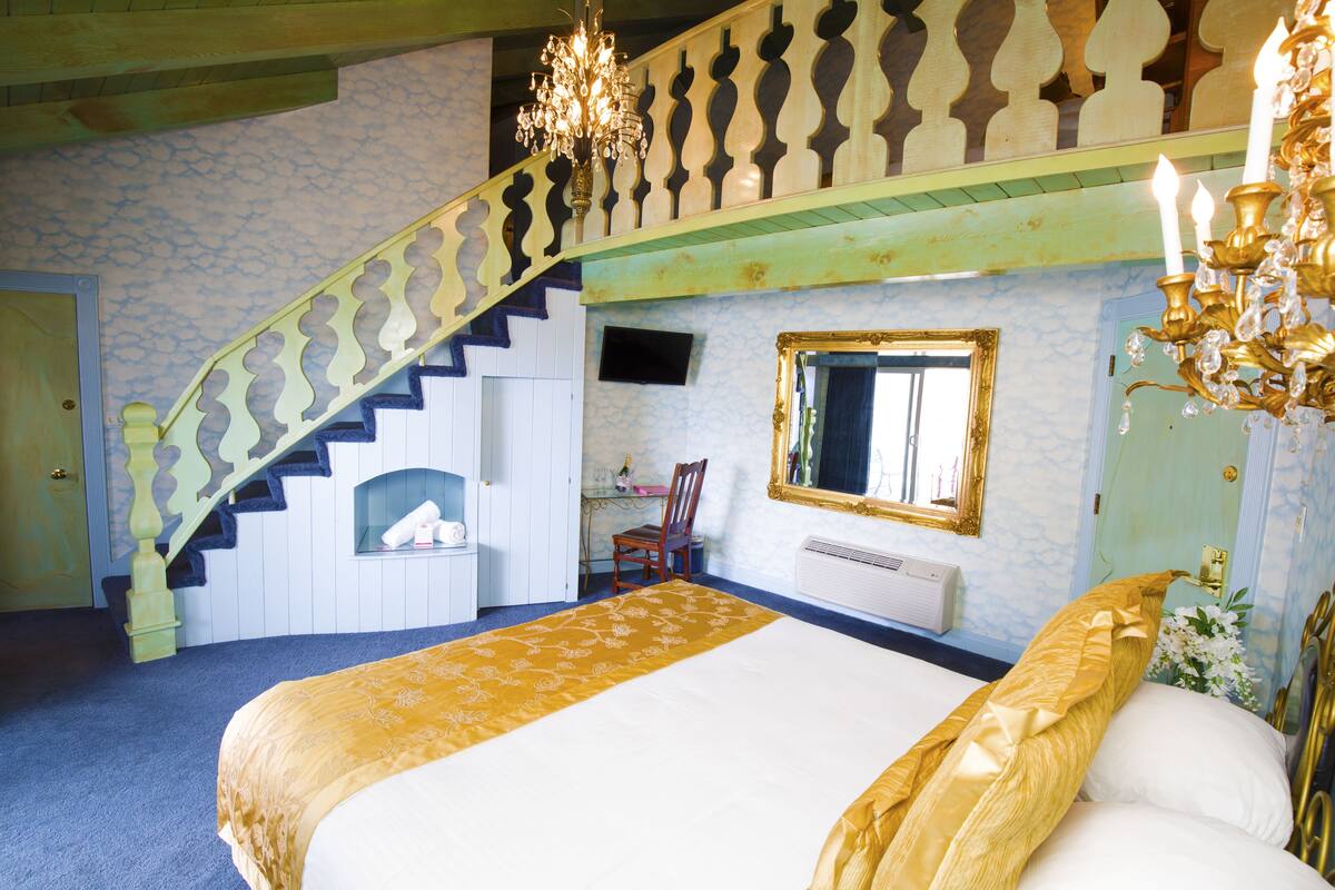 Ein Schlafzimmer mit einem großen Bett, einer Treppe, einem Kamin und einem Spiegel an der Wand.