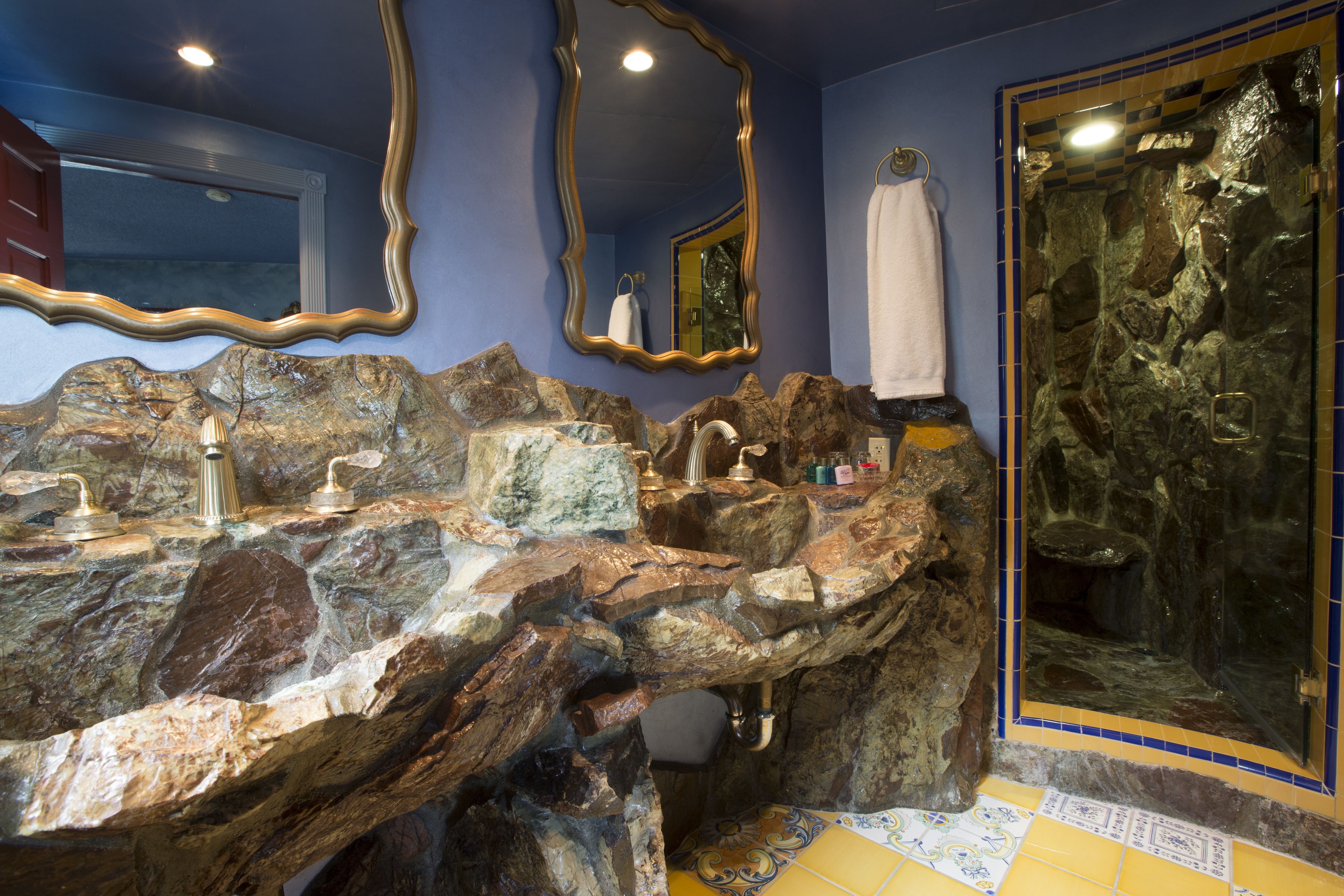 A bathroom with a natural stone sink, a large mirror, and a shower with a stone wall.