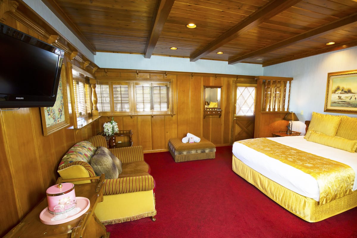 Ein Hotelzimmer mit einem großen Bett, einem Fernseher, Holzvertäfelung, einem roten Teppich und einem Gemälde an der Wand.