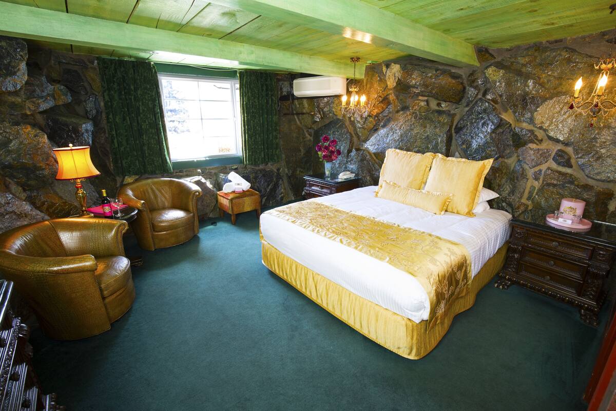 Ein Schlafzimmer mit einem großen Bett, einem Sessel, einem Nachttisch und einer Steinwand.