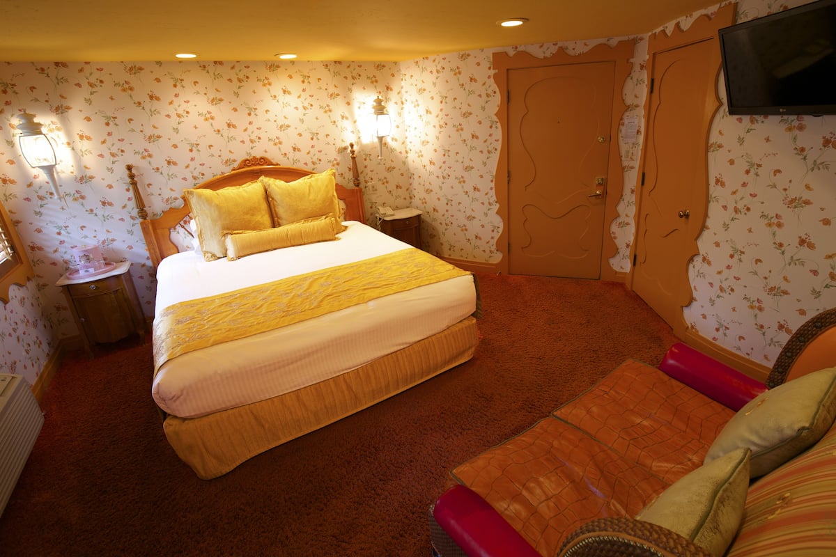 Ein Hotelzimmer mit einem großen Bett, einem kleinen Tisch, einem an der Wand montierten Fernseher und einer Tür mit ungewöhnlichem Design.
