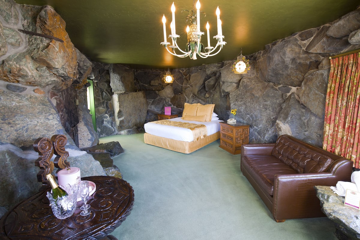 Ein Schlafzimmer mit Steinwand, einem Bett, einem Holzstuhl, einer Ledersofa und einer Chandelieber.