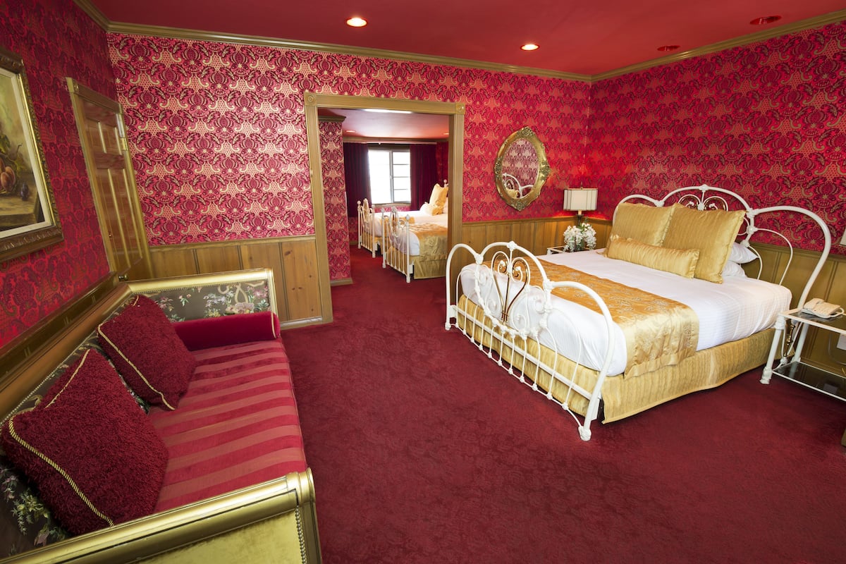 Ein Zimmer mit einem großen Bett, einem kleineren Bett, einer Schlafcouch und einem Spiegel.