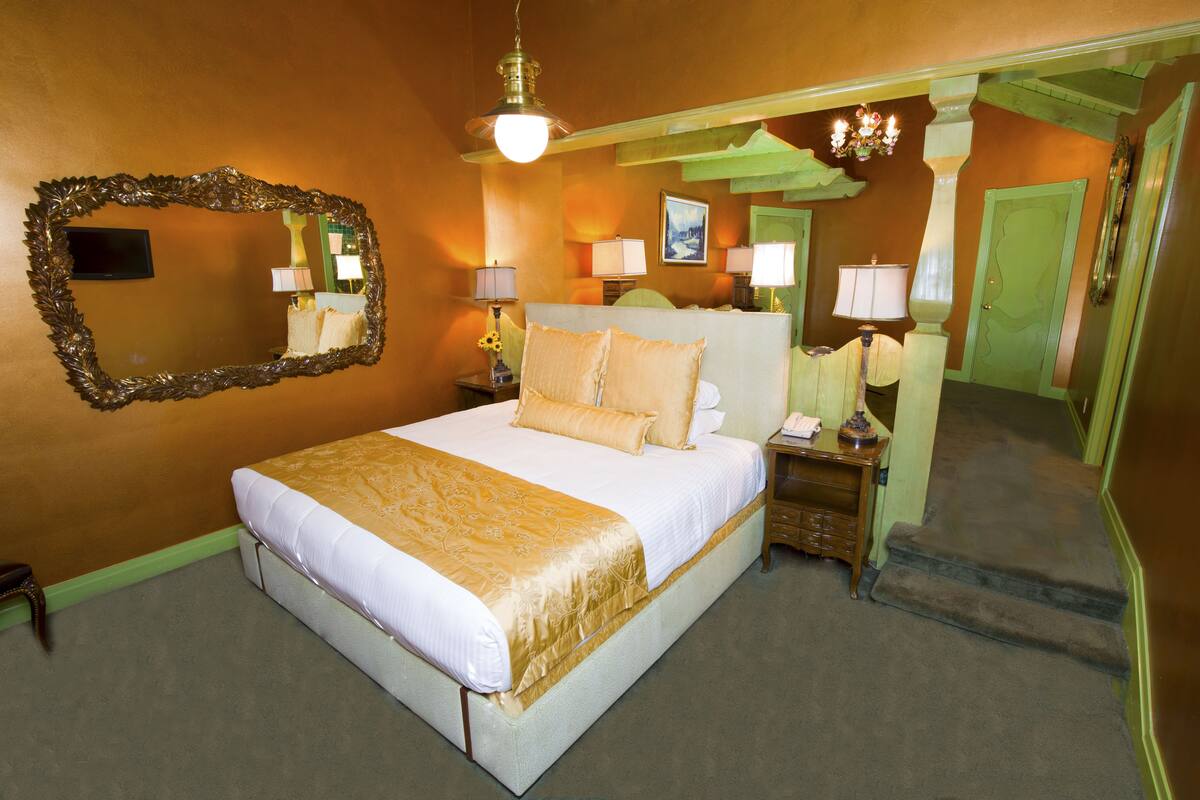 Ein Hotelzimmer mit einem großen Bett, einem Spiegel, zwei Nachttischen mit Lampen und einer Treppe, die in einen anderen Raum führt.