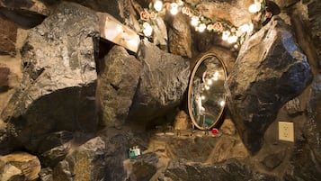 A bathroom with a large mirror, stone walls, and a decorative flower garland.