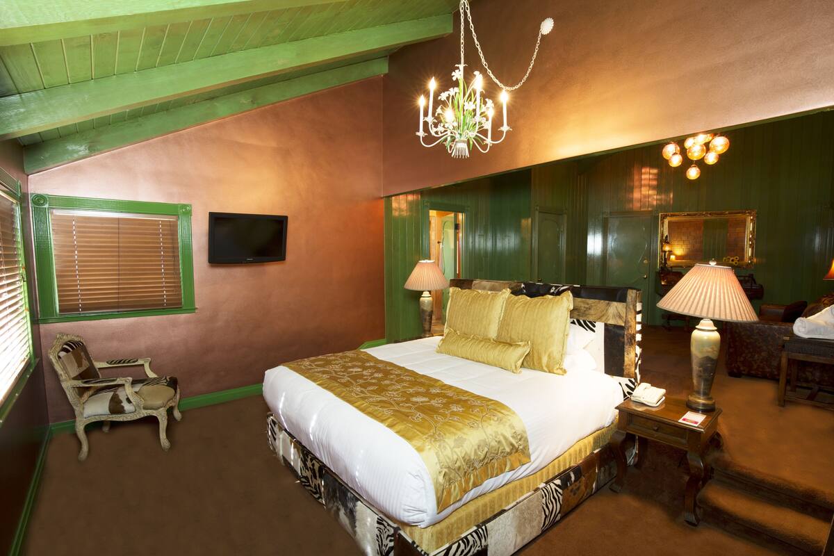 Ein geräumiges Schlafzimmer mit einem großen Bett, einem Sessel, einem Fernseher und einer Chandelier.