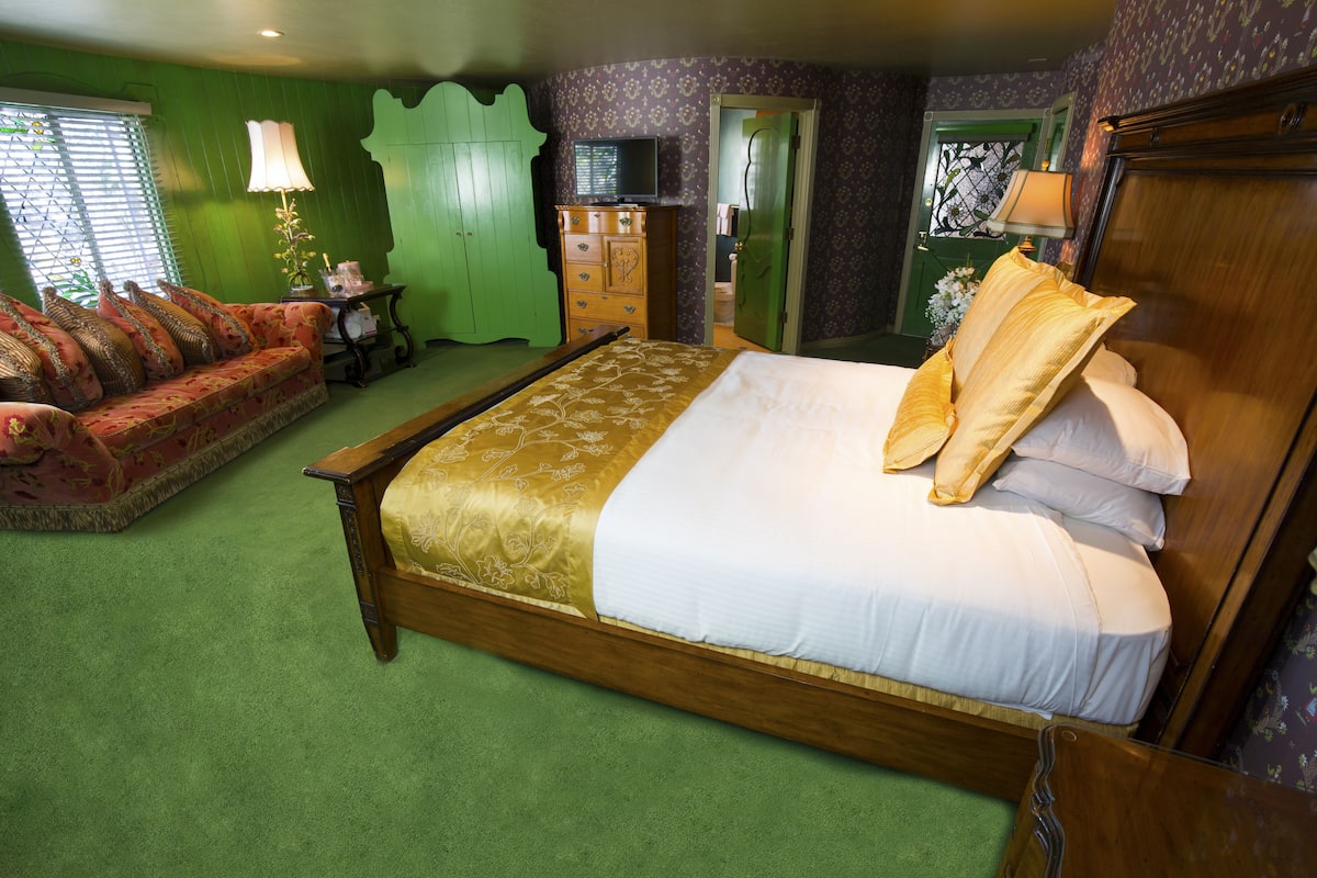 Ein Schlafzimmer mit einem großen Bett, einem grünen Sessel, einer hölzernen Kommode und einem grünen Kleiderschrank.