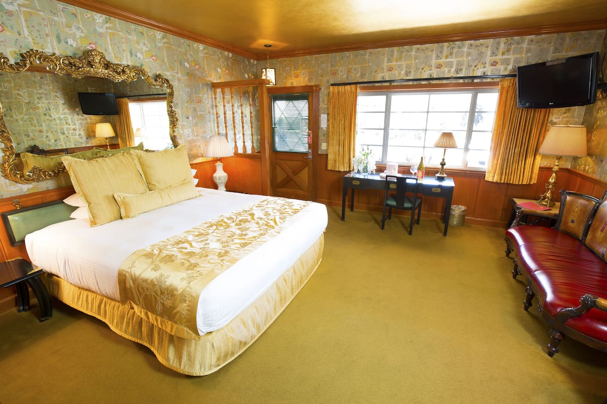 Ein Hotelzimmer mit einem großen Bett, einem Schreibtisch, einem roten Ledersofa, einem Fernseher und einem Fenster mit Vorhängen.