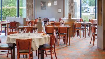 Ein Restaurant mit mehreren Tischen und Stühlen, großen Fenstern und Blick ins Freie.