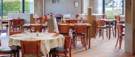 A restaurant with multiple tables and chairs, large windows, and a view of the outdoors.