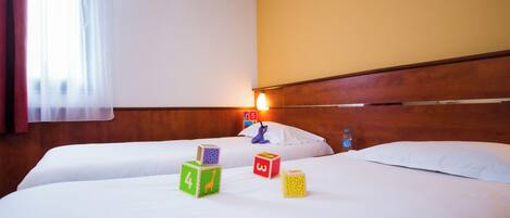 Habitación de hotel con dos camas, cabecero de madera, ventana con cortinas y lámpara fijada a la pared.