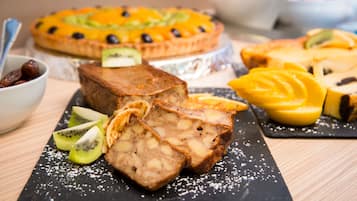 A dessert platter with various fruit-topped cakes and a loaf of bread, served on a black slate board.