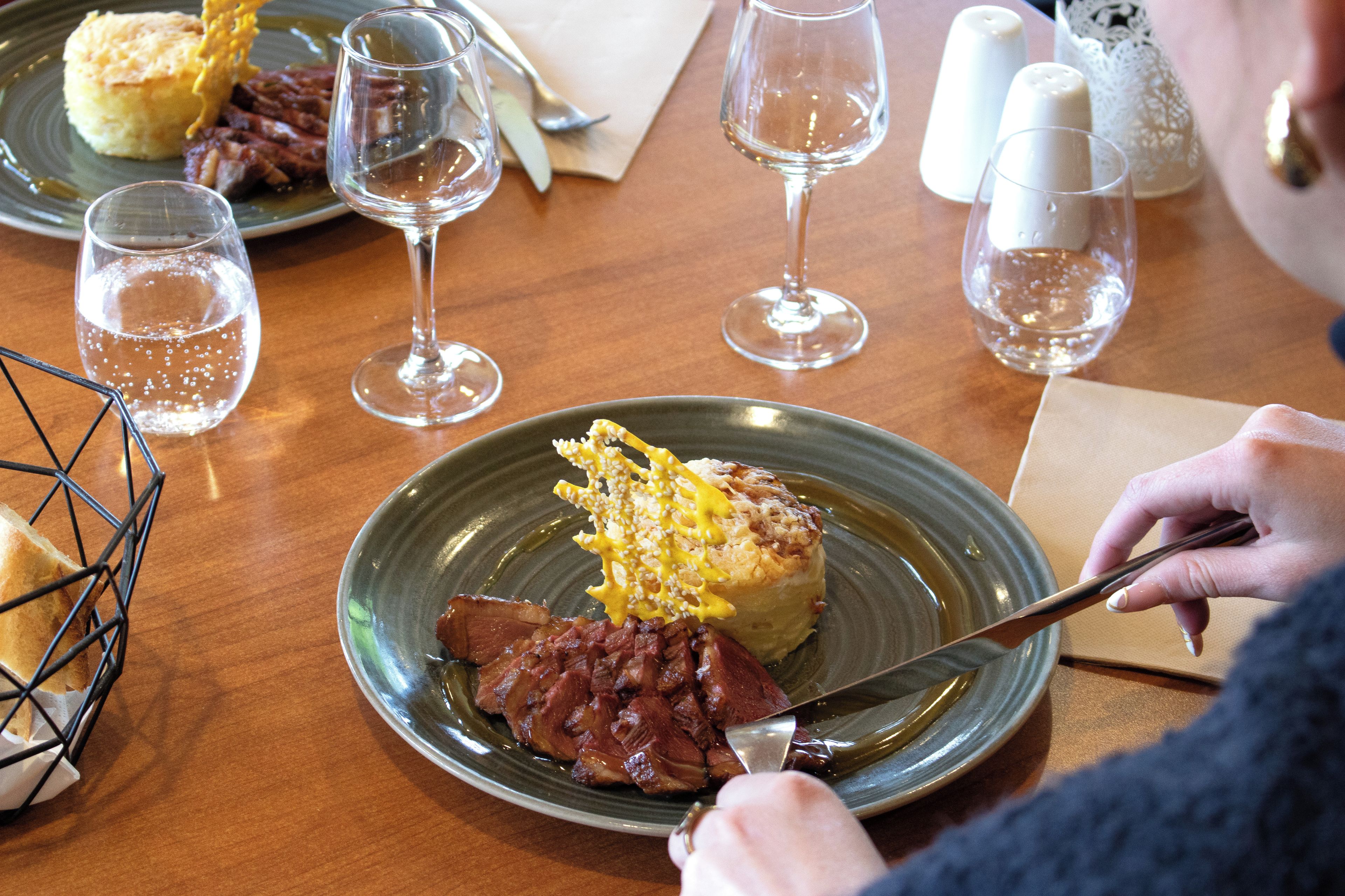 A dining table with plates of food, glasses of water, and a person using a knife.