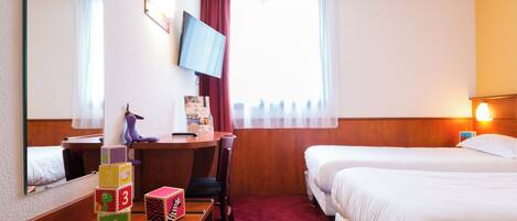 A hotel room with a desk, a television, a bed, and a window with curtains.