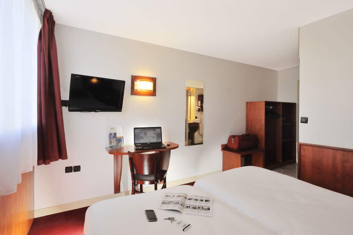 Une chambre d’hôtel équipée d’un lit, d’un bureau avec un ordinateur portable, d’une télévision, d’un miroir et d’une armoire.